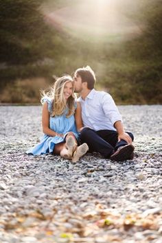 a man and woman are sitting on the ground in front of some rocks, smiling at each other