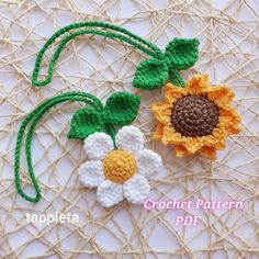 two crocheted flowers are sitting on a piece of yarn with green leaves and brown centers