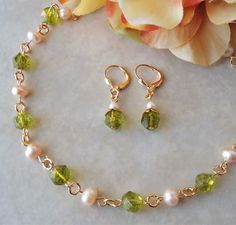 "This classic beaded necklace features beautiful green Peridot gemstones and ivory freshwater pearls. Necklace is finished with a lobster closure. The necklace measures 18 inches in length. This simple yet elegant pair of earrings features green Peridot gemstone drop with a tiny freshwater pearl. Hanging from a surgical steel lever-back, it measures 1.25 \" in length. Earrings are light weight and sway gracefully as you move about your day. This beautiful necklace is unique, feminine and eye-cat Green Single Strand Jewelry For Wedding, Green Pearl Jewelry For May Birthstone, Gold Peridot Necklaces For Wedding, Green Pearl Necklace With Round Beads And Pearl Drop, Green Pearl Dangle Jewelry, Green Pearl Charm Jewelry For Wedding, Green Pearl Drop Jewelry With Round Beads, Green Pearl Round Beads Jewelry, Peridot Gemstone Bead Necklace For Gift