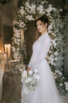 a woman in a white wedding dress holding a bouquet and standing next to a table with candles