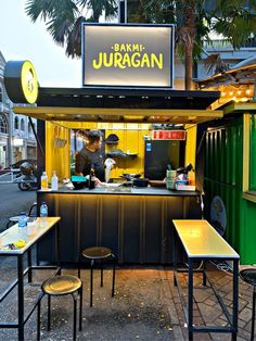 an outdoor food stand with tables and stools on the side of the street in front of it