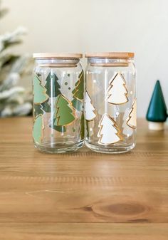 two glass jars sitting on top of a wooden table next to a small christmas tree