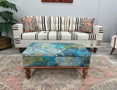 a living room with a couch, ottoman and rug on the floor in front of a painting