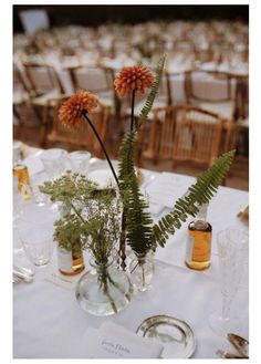 an arrangement of flowers in vases on a white table cloth with chairs and tables