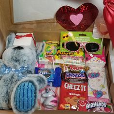 a teddy bear sitting in a cardboard box filled with candy and other items for valentine's day