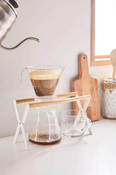 coffee being poured into a glass cup from a pour - over machine on top of a counter