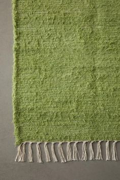 a green rug with fringes on the bottom and one in the middle, sitting on top of a gray floor