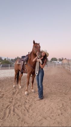 a woman is standing next to a brown horse in the sand with a rope around her neck