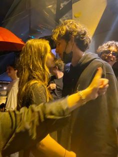 two people standing next to each other in front of a crowd with an orange umbrella