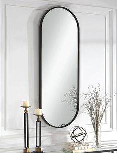 a mirror sitting on top of a wall next to a table with candles and a vase