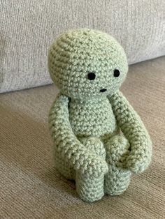 a crocheted stuffed animal sits on the floor in front of a couch with its eyes closed