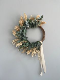 a wreath hanging on the wall with dried grass and eucalyptus leaves attached to it's side