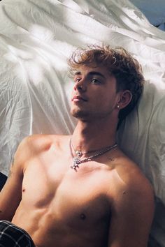 a shirtless man laying in bed wearing a necklace