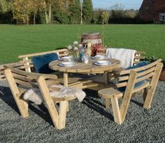 a wooden table and chairs sitting on gravel in front of a green field with trees