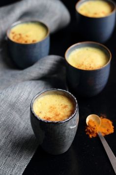 three cups filled with food sitting on top of a table next to two spoons