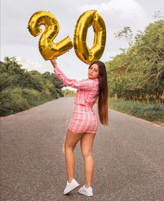 a woman in a pink dress holding up two gold balloons that say 20 and the number twenty