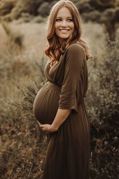 a pregnant woman smiles while standing in tall grass