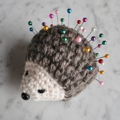 a crocheted hedge with colorful pins on it's head sitting on a marble surface