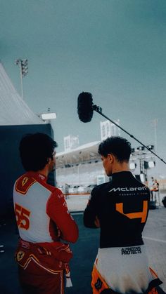 two men standing next to each other in front of a camera on top of a building