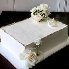 a square cake with white flowers on top and gold trim around the edges is sitting on a table