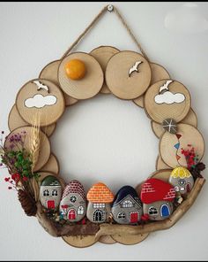 a wreath made out of wooden slices with houses and birds painted on the front, hanging from a wall