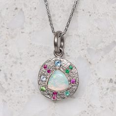 Our pebble collection of raw, rough, beaten metals set with precious gems. Perfectly imperfect and all one of a kind. A crystal opal is surrounded by pink sapphires, emeralds and aquamarines and is set into a pebble disc necklace. Pebble measures 13.5mm round approx. Pendant weighs 4.8g approx. If ordering with a chain, the chain measures 45cm. Please note if ordering the white gold it is raw with a matte finish and not rhodium plated. Opal Multi-stone Pendant Necklace, Gemstone Jewelry With Ethiopian Opal Round Pendant, Ethiopian Opal Gemstone Pendant Jewelry, Silver Multi-stone Ethiopian Opal Jewelry, Pebble Collection, Painters Palette, Crystal Opal, Aqua Marine, Disc Necklace