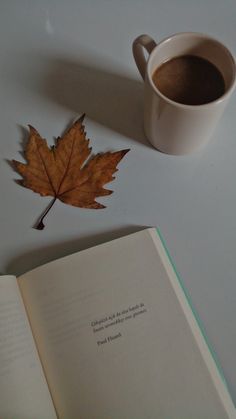 an open book with a leaf on it next to a cup of coffee