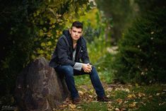 a young man sitting on top of a rock in the grass next to some trees