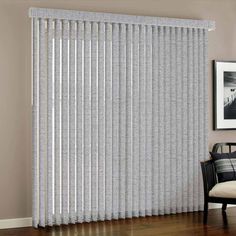 a living room with white vertical blinds on the wall and wood flooring in front of it