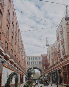 people are walking down an alley way with buildings in the background and lights strung overhead