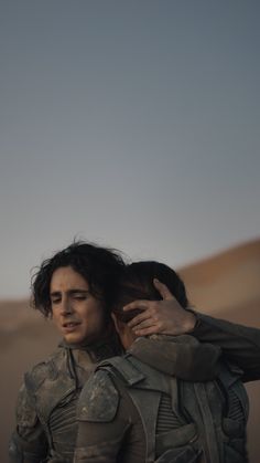 two people standing in the desert with their backs to each other and one person holding his back