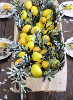 a wooden table topped with lots of lemons and greenery on top of plates