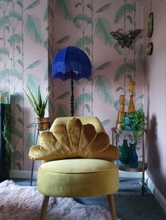 a yellow shell chair sitting in front of a pink wall with palm leaves on it