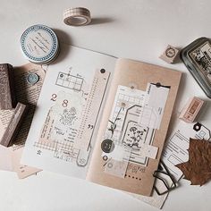 an open book with stamps, tape and other items on it sitting on a table