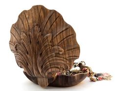 a wooden shell shaped dish with beads in the bottom and chain hanging from it's side