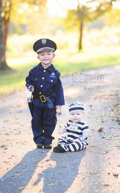 two young boys dressed in police uniforms standing next to each other on a dirt road