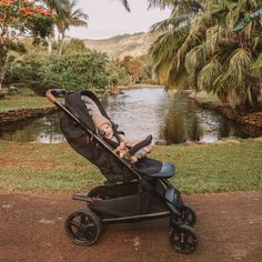 a baby laying in a stroller next to a pond