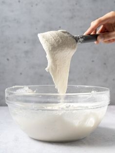 someone using a spatula to mix ingredients in a glass bowl on a white table