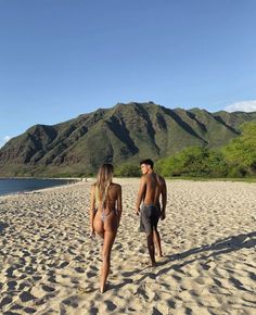 a man and woman walking on the beach with mountains in the backgrouds