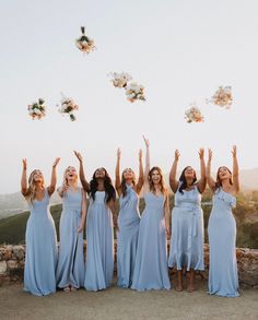 a group of women standing next to each other in front of a stone wall holding flowers