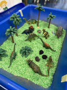 a blue plastic container filled with fake dinosaurs and palm trees on top of green grass