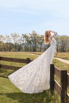 a woman in a long white dress leaning on a fence with her hands behind her head