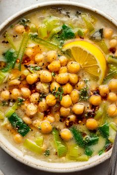 a bowl filled with chickpeas, spinach and lemon wedges next to a spoon