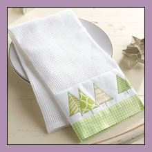 a green and white dish towel with trees on it next to a plate that has a napkin holder