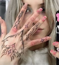 a woman holding her hands up to her face with pink and black designs on it