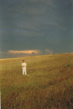 a man standing in the middle of a field under a dark sky with storm clouds