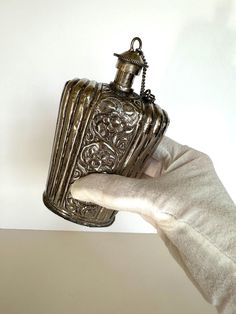 a hand holding an antique silver flask shaped like a bottle with a chain hanging from it