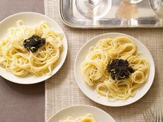 three plates of spaghetti with black cauliflower on them and silverware next to it