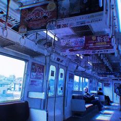 a man sitting on a subway car next to a window filled with signs and advertisements