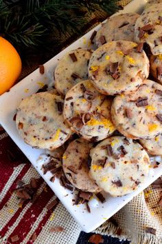 cookies with orange zest and chocolate chips on a white plate next to an orange